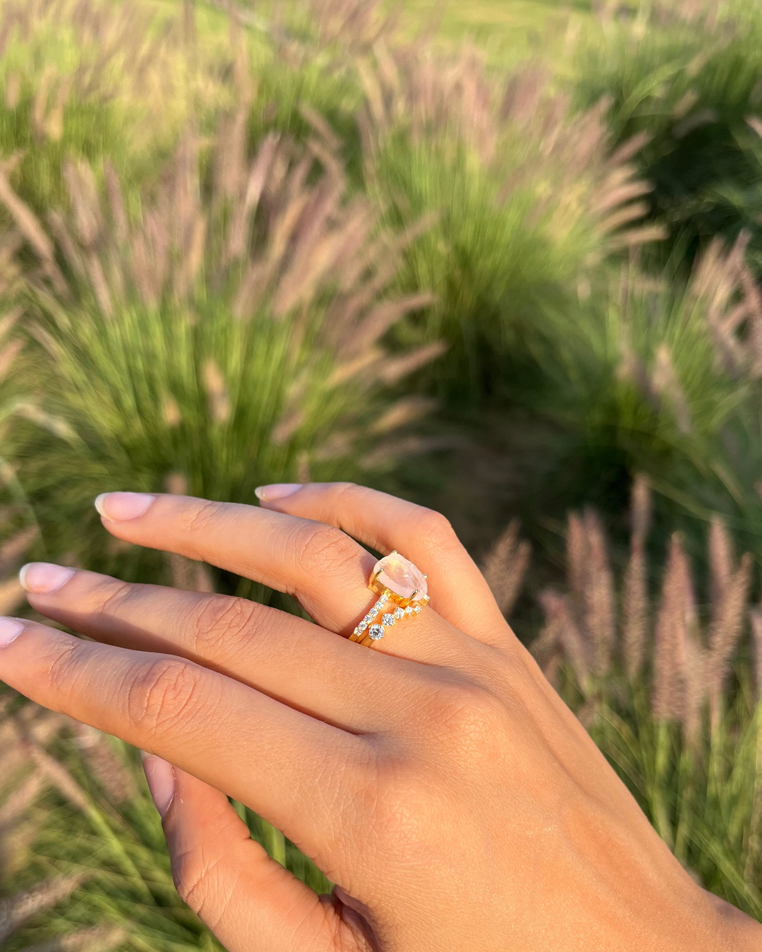 Hand wearing a ring with a floral design in a field of tall grass.