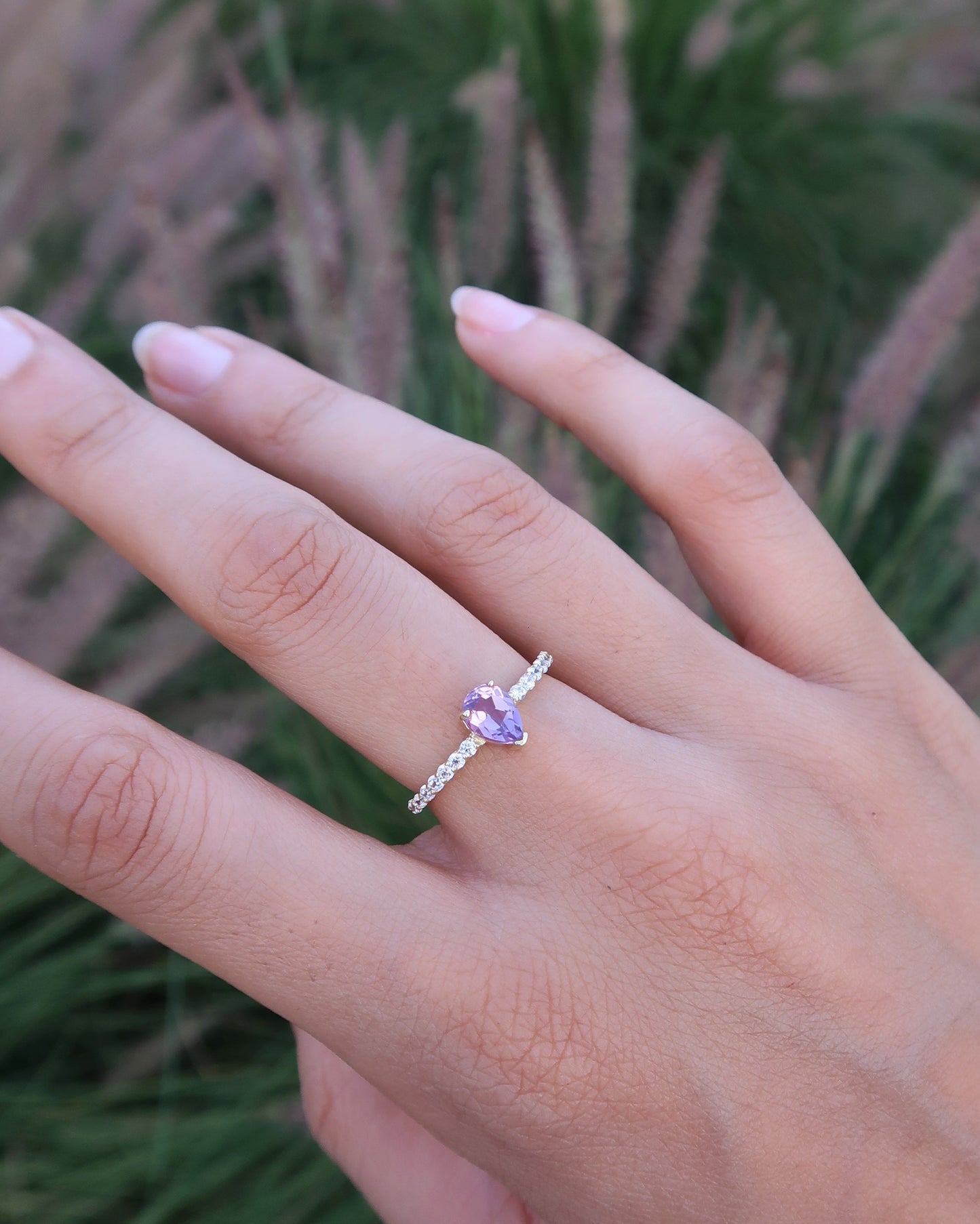Hand wearing a ring with a purple gemstone against a blurred green background