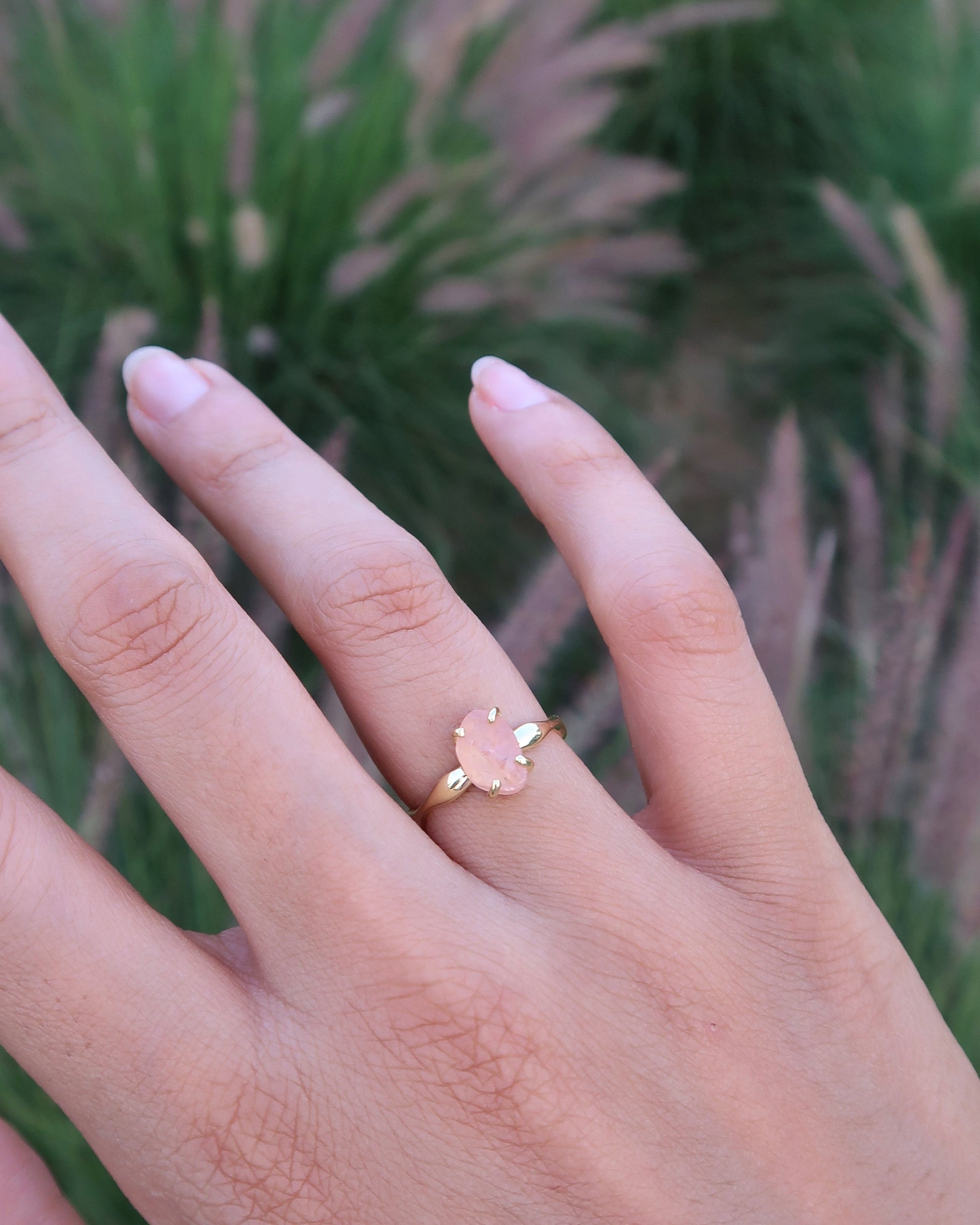 Hand wearing a gold ring with a small diamond, set against a blurred natural background